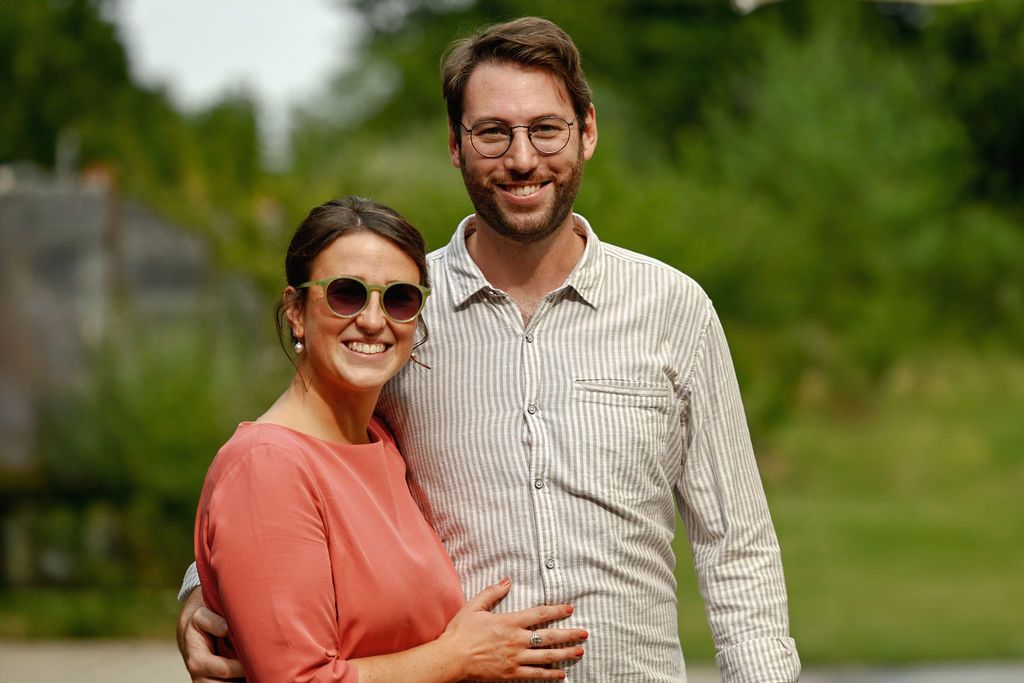 A couple laughs together outdoors while walking in a park setting on a sunny day.
