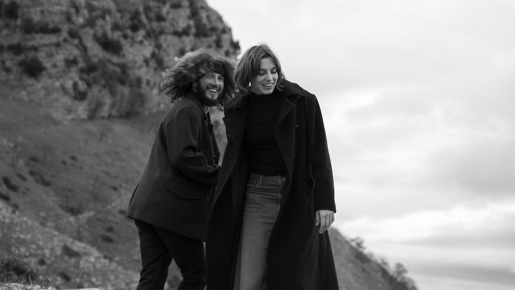 A couple embraces while standing on a rocky mountain slope in black and white.