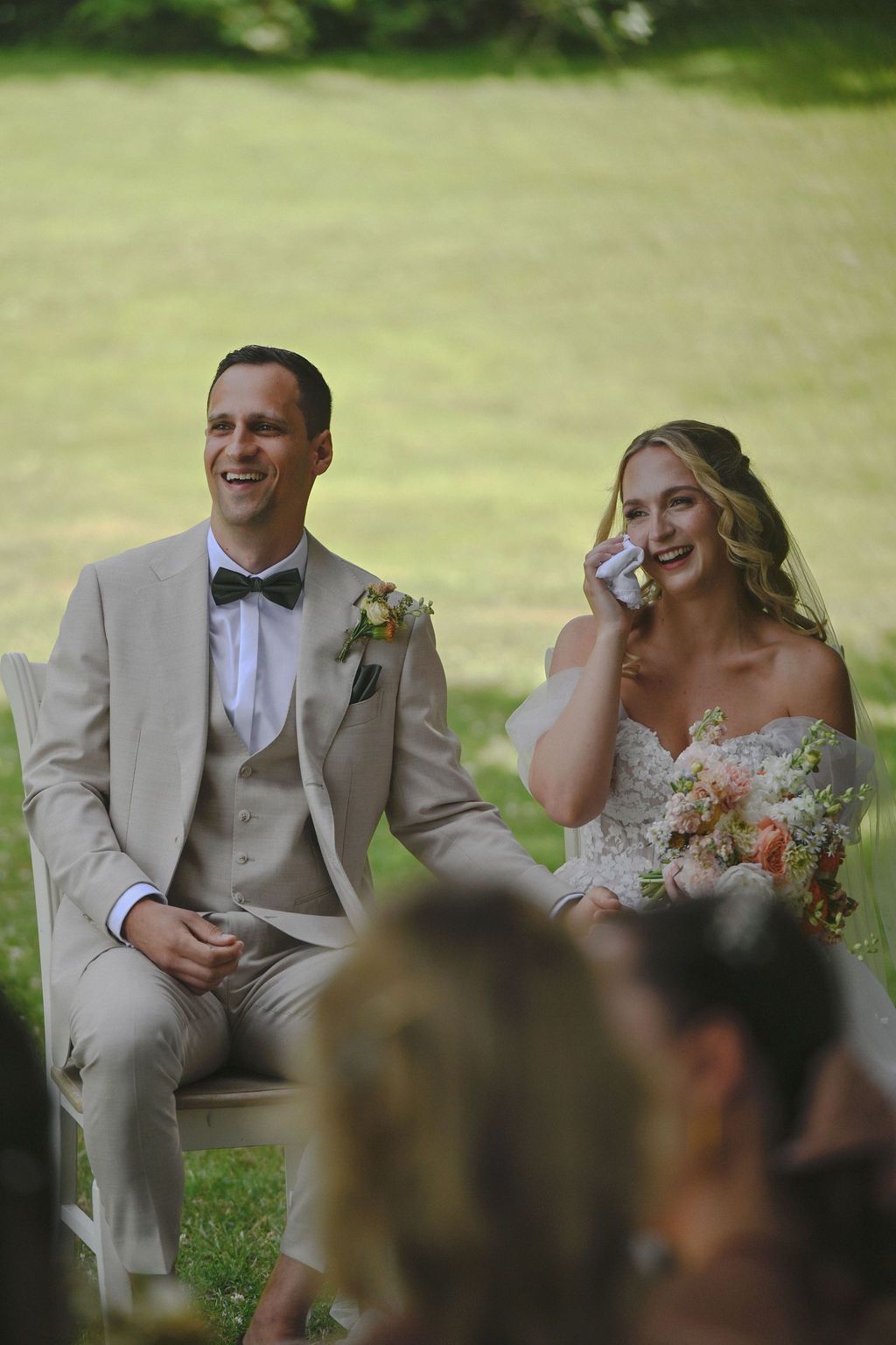 A bride and groom share a joyful moment during their outdoor wedding ceremony on a sunny day.