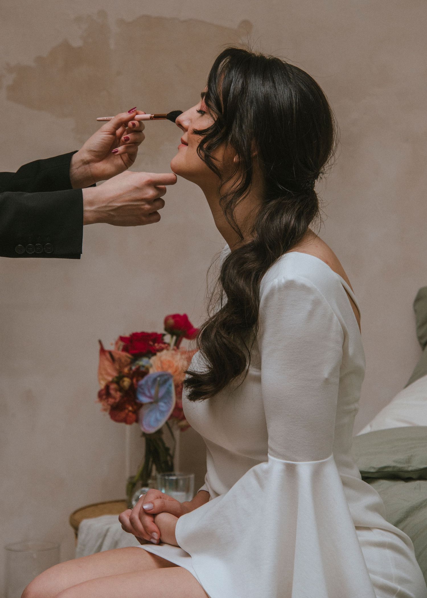 Elegant wedding preparation scene with makeup application and floral bouquet.
