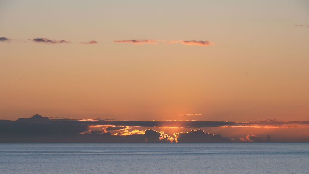 A stunning panoramic sunset over calm ocean waters with vibrant orange clouds reflecting on the horizon.