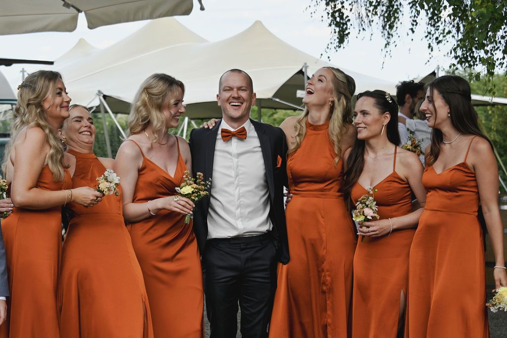 Wedding party in burnt orange bridesmaid dresses laughing together outdoors during photo session.
