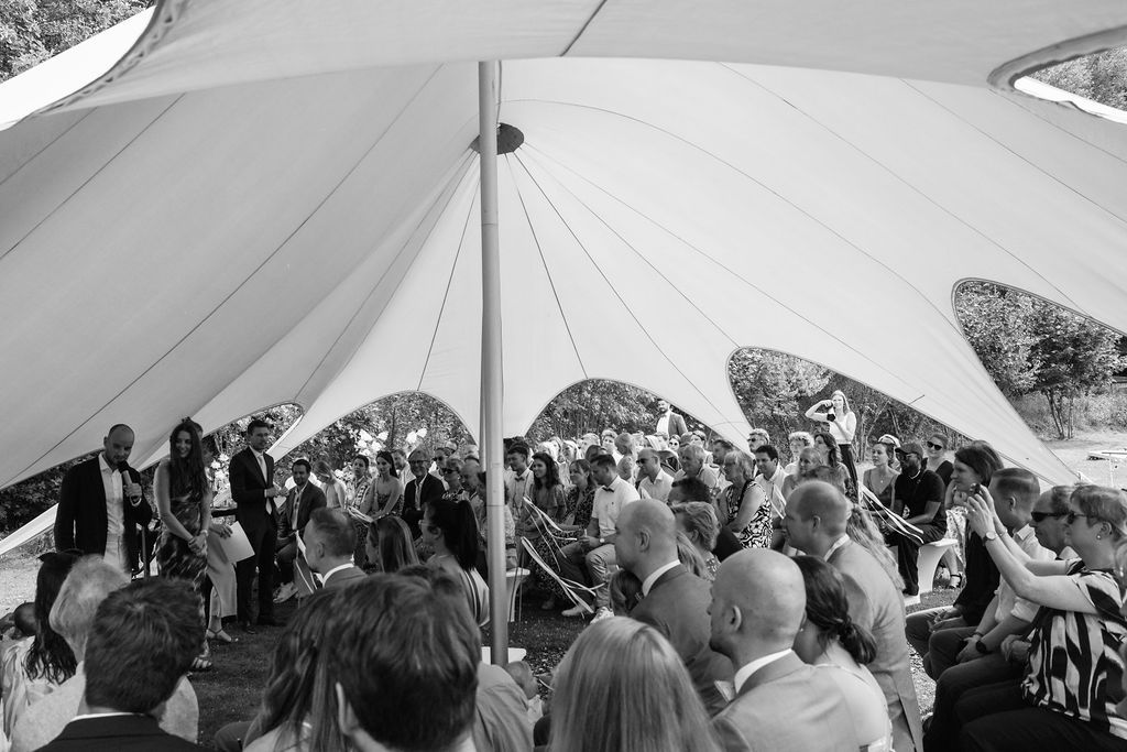 Large group of people gathered under a white tent canopy for an outdoor event.