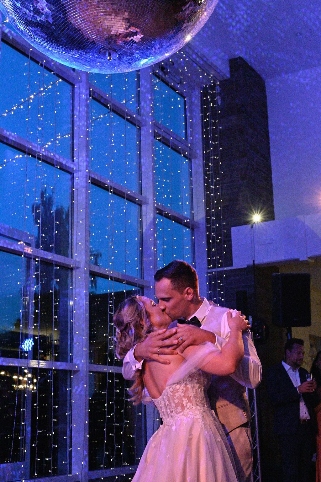 A couple shares a romantic dance moment under blue lighting and string lights at their wedding reception.