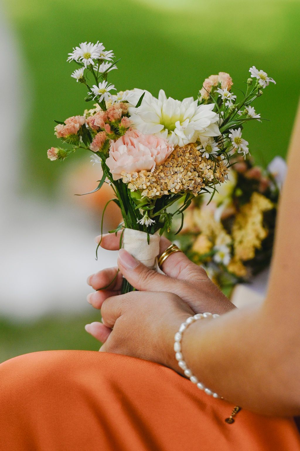 A delicate bouquet of white daisies, pink roses and baby's breath held by hands adorned with a pearl bracelet.
