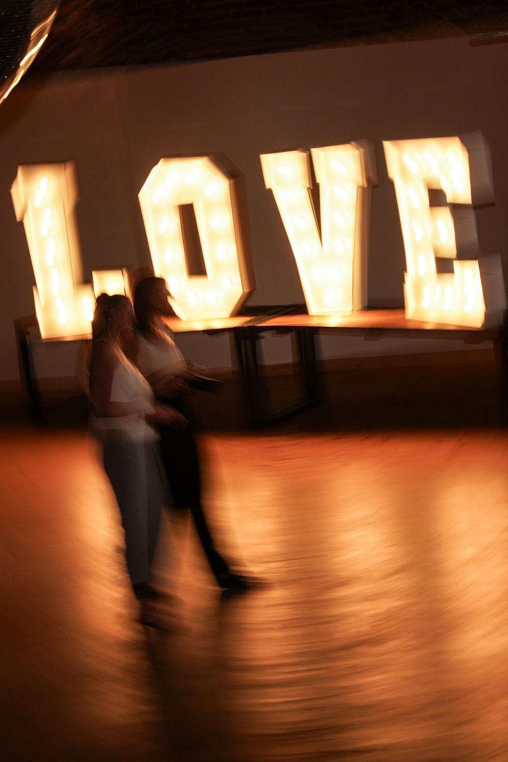 Motion blur captures a person walking past illuminated letters on a dark wooden floor creating an artistic effect.