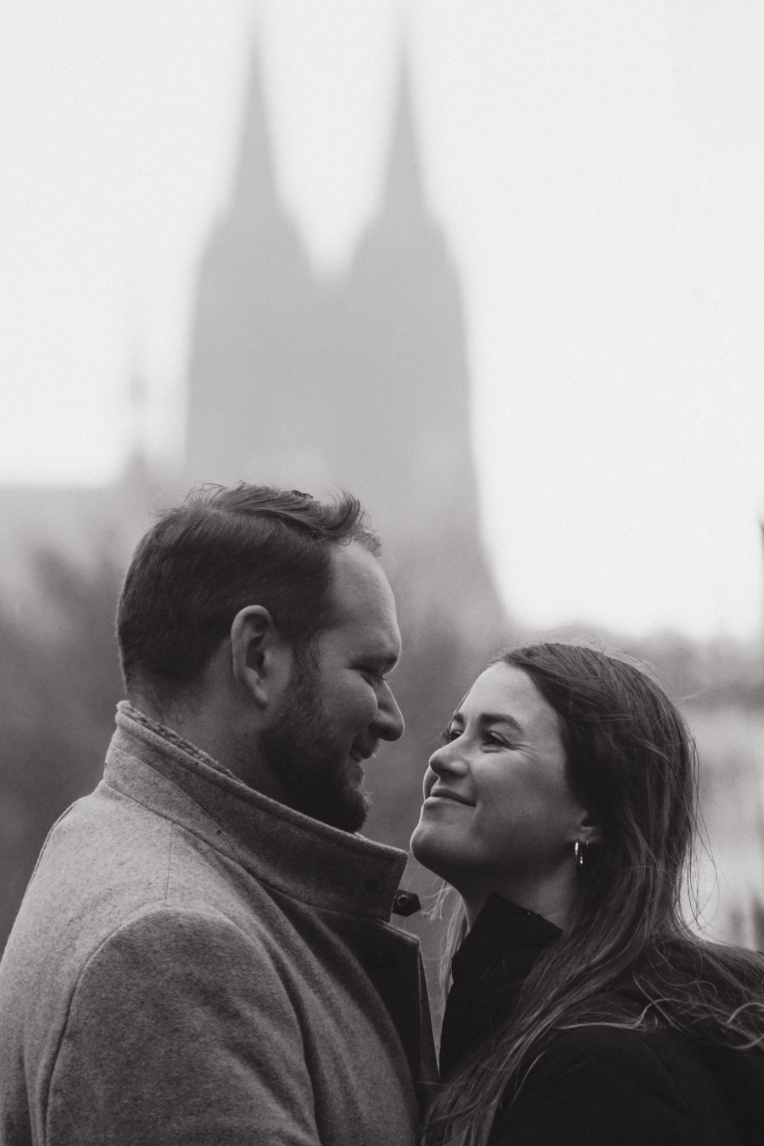 An intimate black and white portrait of a couple with a gothic cathedral silhouette behind them.