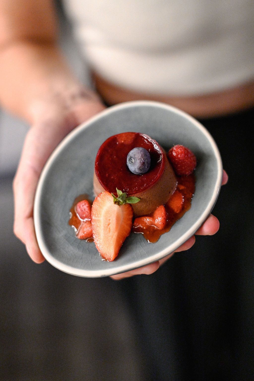 Hands holding small white plates with fresh strawberries and blueberries arranged in an artistic sequence.