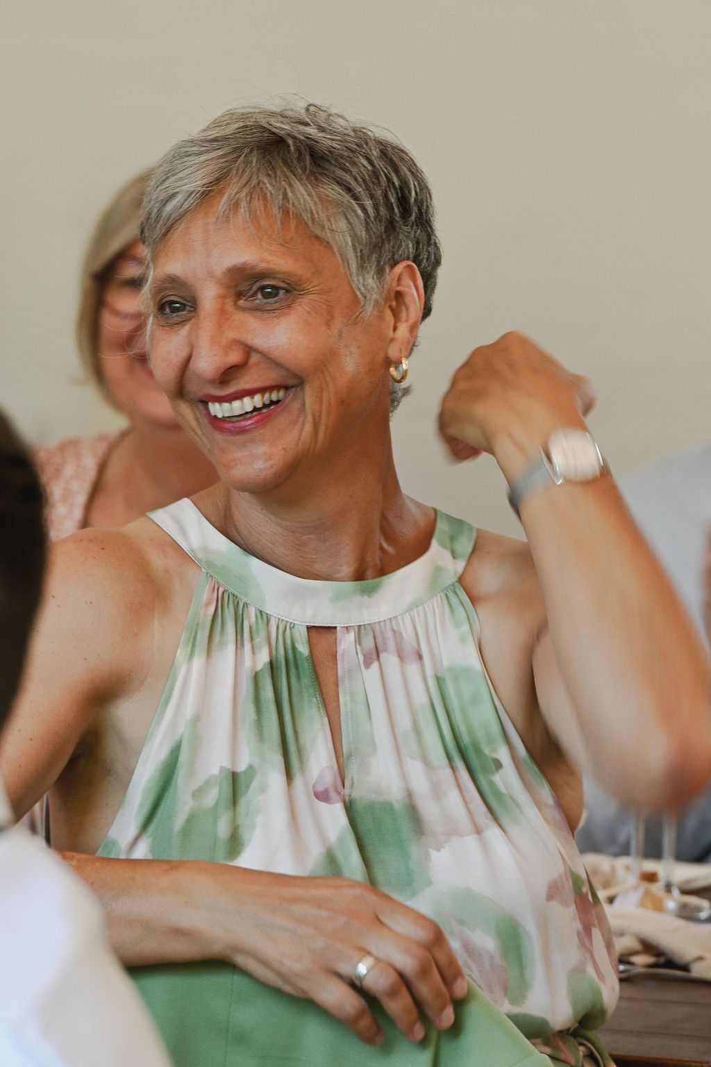 Someone wearing a green and white sleeveless top smiles warmly during what appears to be a social gathering.