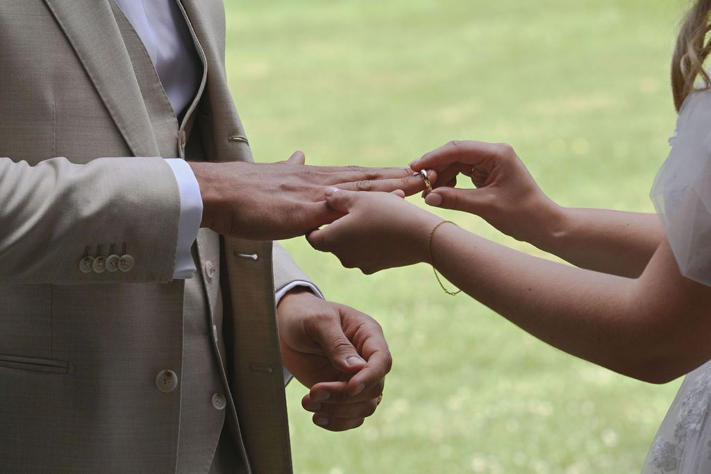A series of hands exchanging wedding rings during an outdoor ceremony on a sunny day.