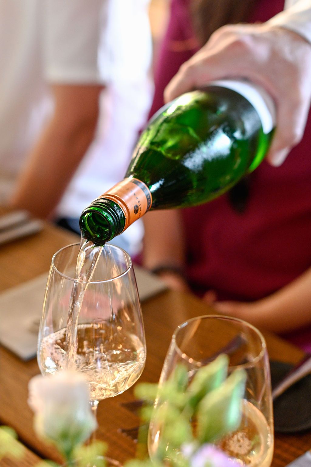 White wine being poured into elegant wine glasses at a tasting event.