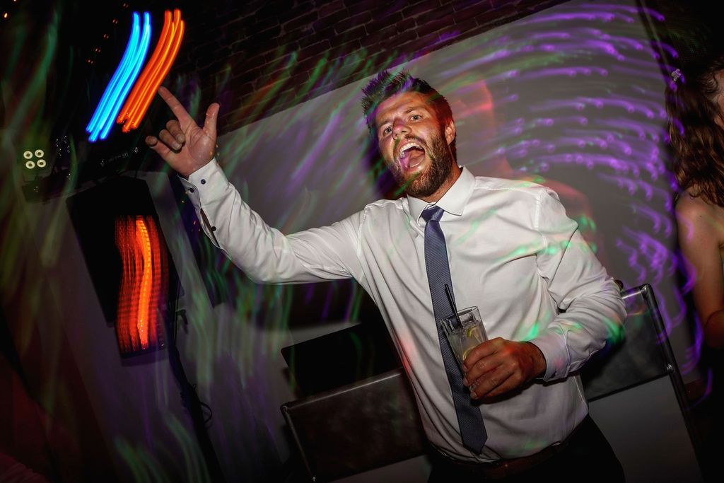 Wedding guests dancing and celebrating on a dance floor with colorful purple lighting and neon accents in the background.