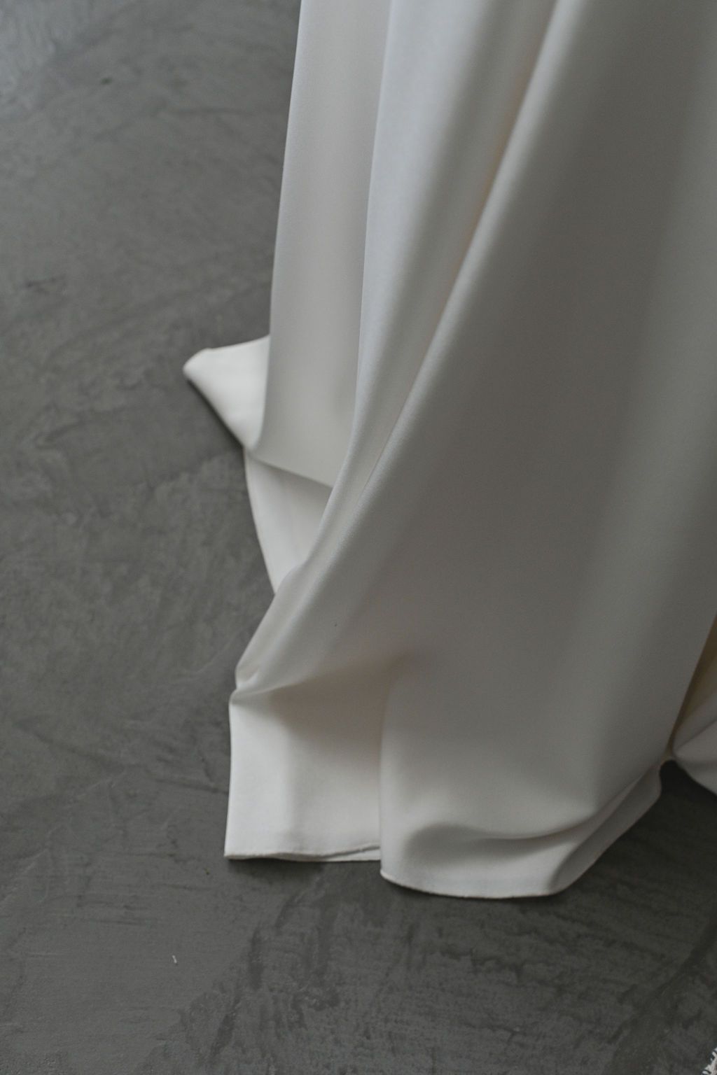 The hem of a flowing white dress or gown against a grey floor.