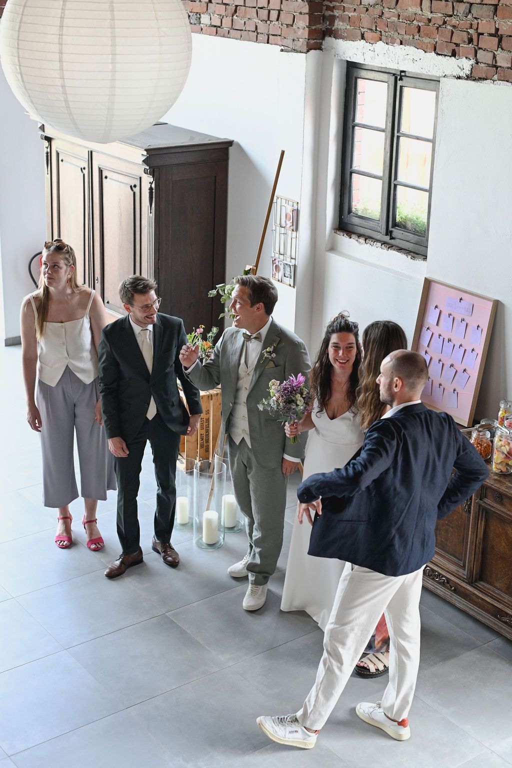 People in formal attire dance and interact with large white paper lanterns in a spacious indoor setting.