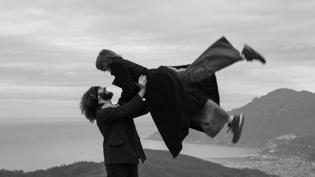 A couple embraces in a dramatic dance pose against a scenic mountain backdrop.