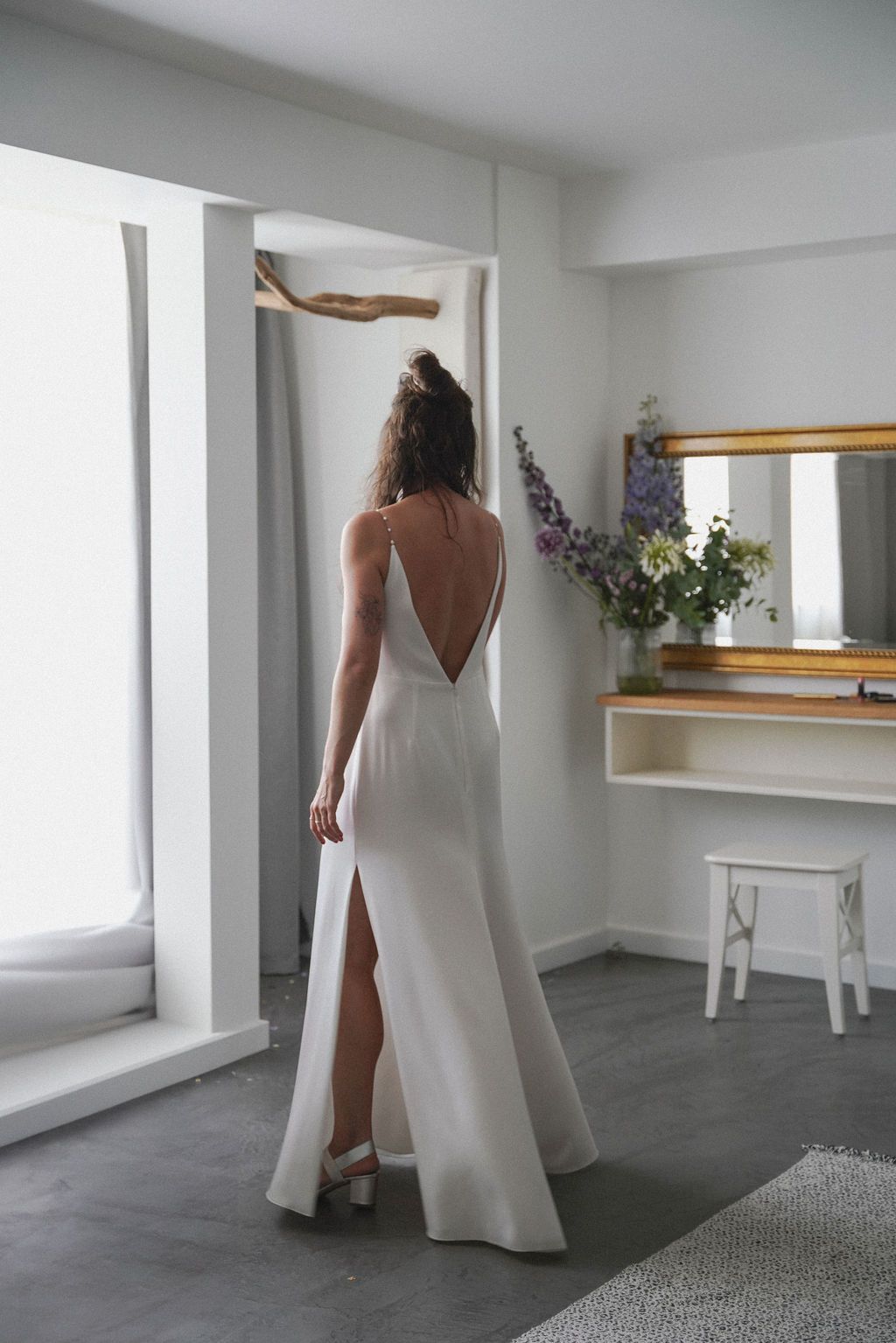 A person wearing a white flowing wedding dress poses in a minimalist white studio space with wooden accents.