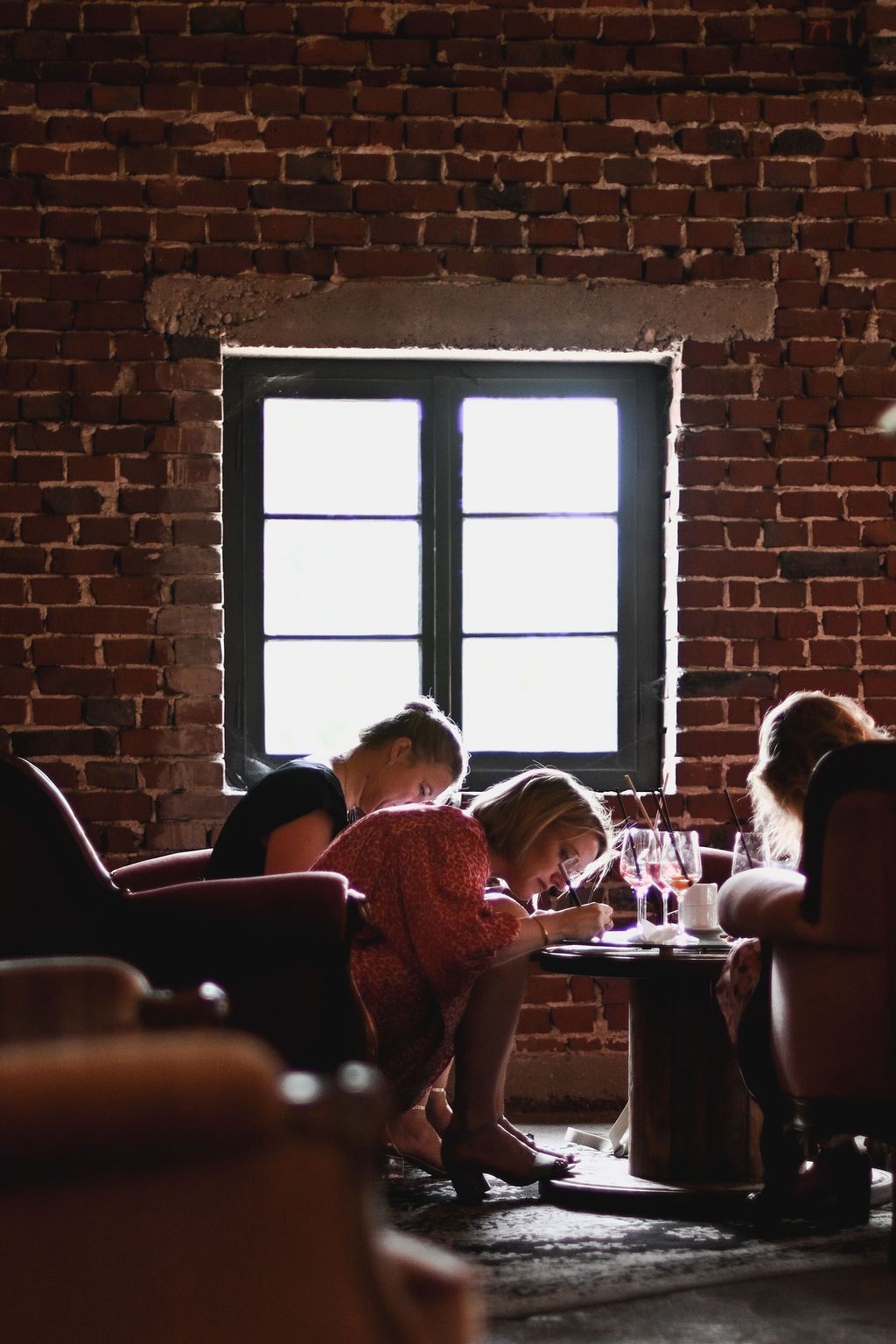 A dark brick-walled restaurant interior with silhouetted diners seated by windows creating a moody ambiance.