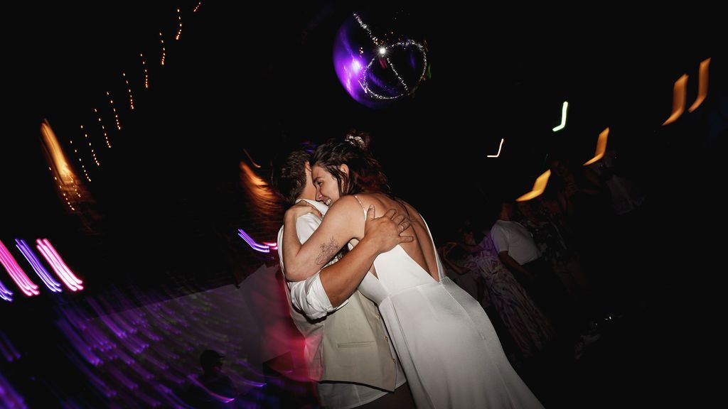 A couple dancing together at a wedding reception with colorful purple and orange lighting effects in the background.