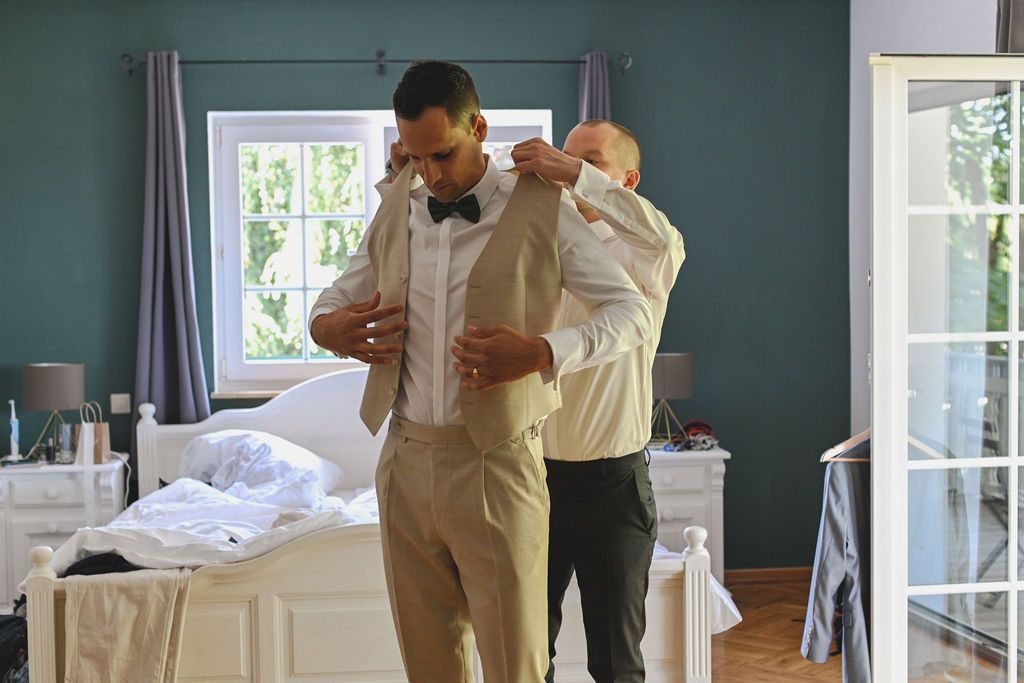 A group of people in formal attire dance together in an elegant room with white French doors and teal walls.