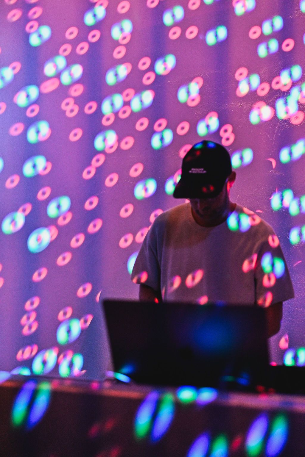 DJ performs at a nightclub with colorful blue and pink bubble-like light projections in the background.