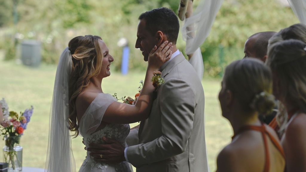 Guests watch an emotional moment during an outdoor wedding ceremony under a white fabric arch.