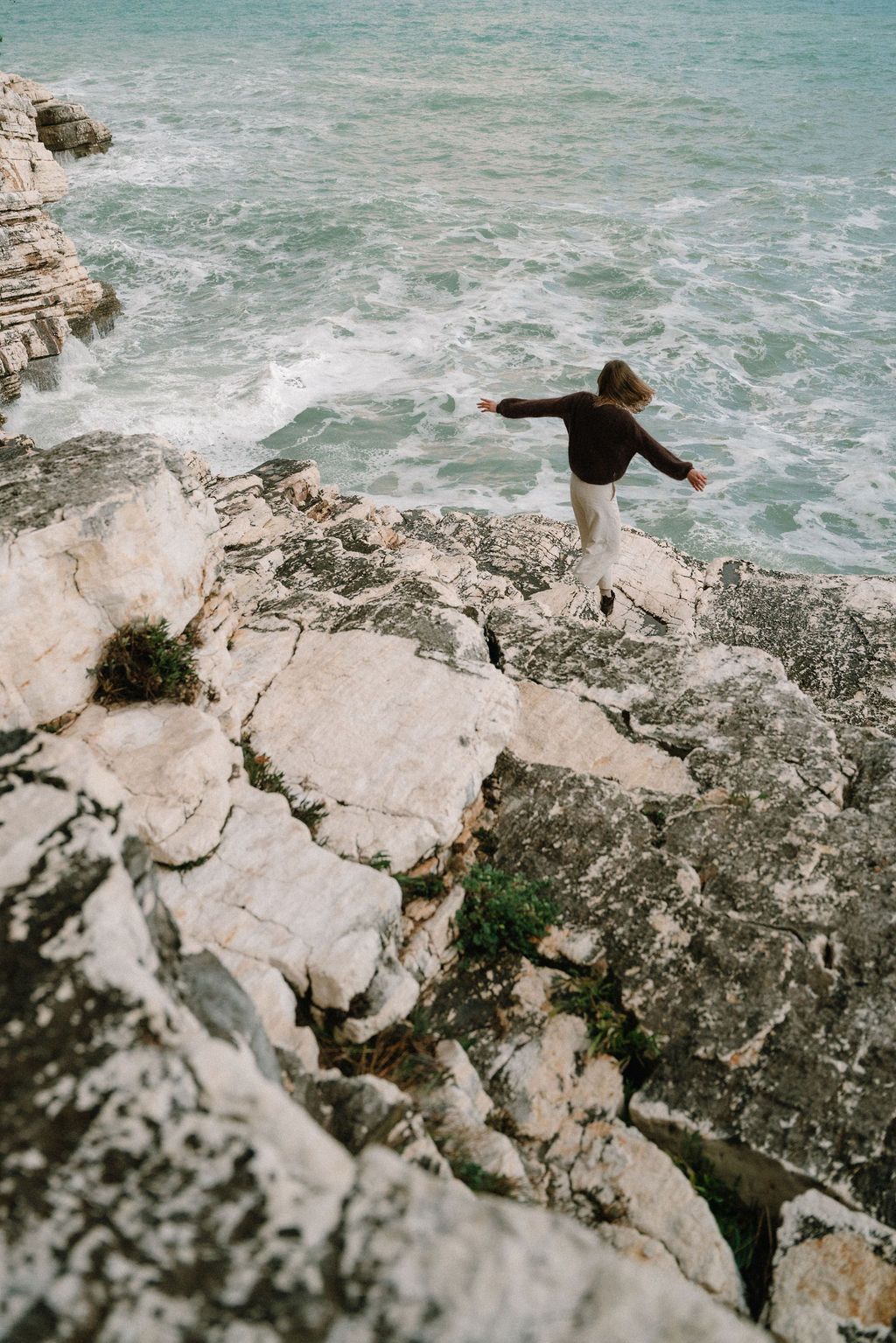 Turquoise ocean waves crash against white limestone cliffs on a rugged rocky coastline.