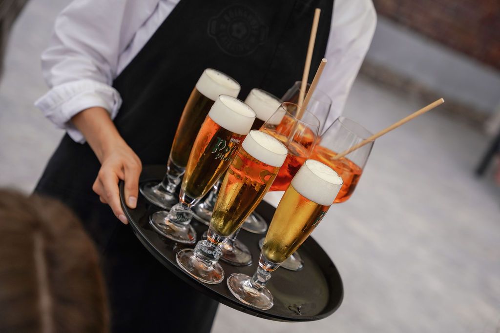 Multiple glasses of beer and cocktails arranged on a dark serving tray at what appears to be a social event.