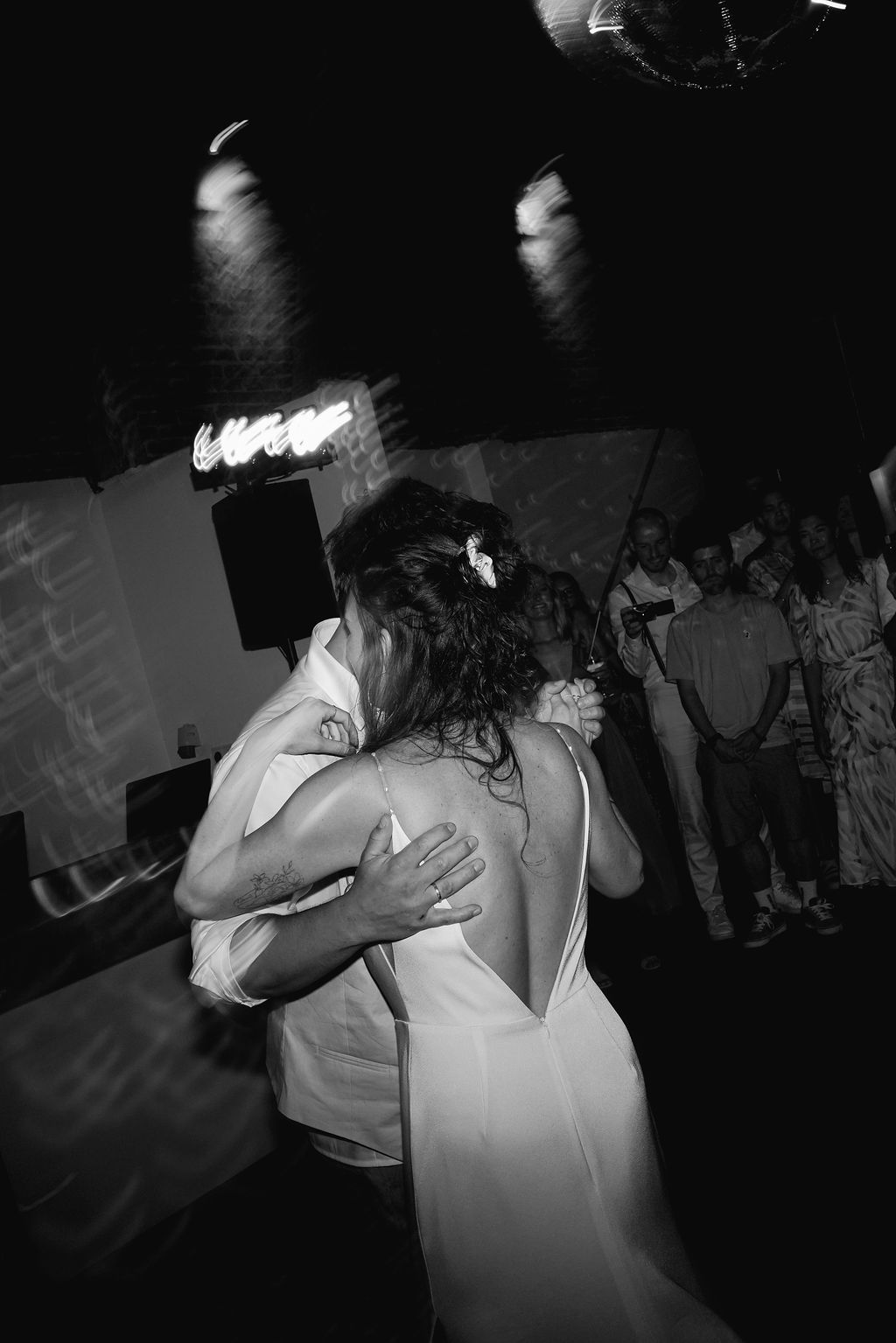 A black and white photo of a couple dancing intimately at a nightclub under disco lighting.