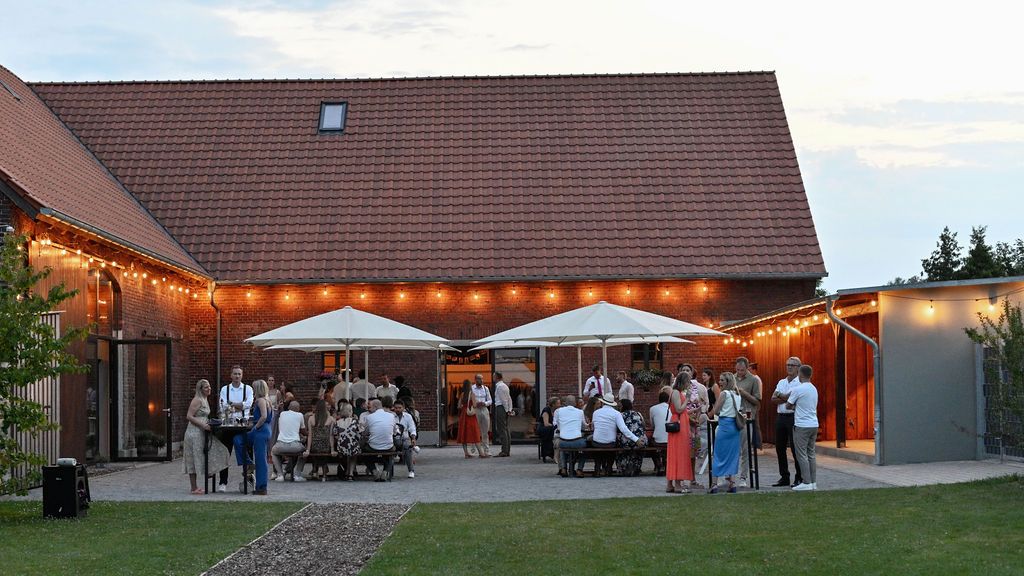 A panoramic view of a rustic barn venue with string lights illuminating the outdoor patio space at dusk.
