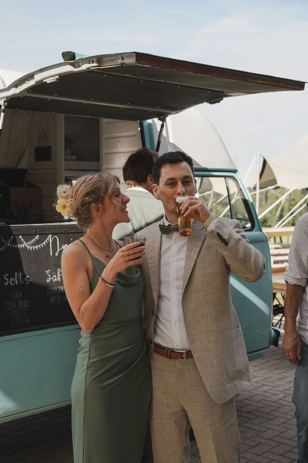 A couple enjoys drinks together at a vintage turquoise food truck during an outdoor event.
