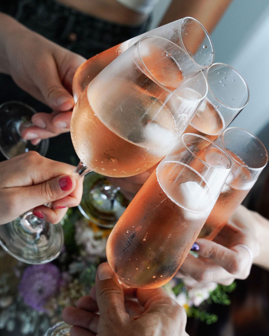 Multiple hands holding wine glasses filled with rose wine in a toasting gesture.