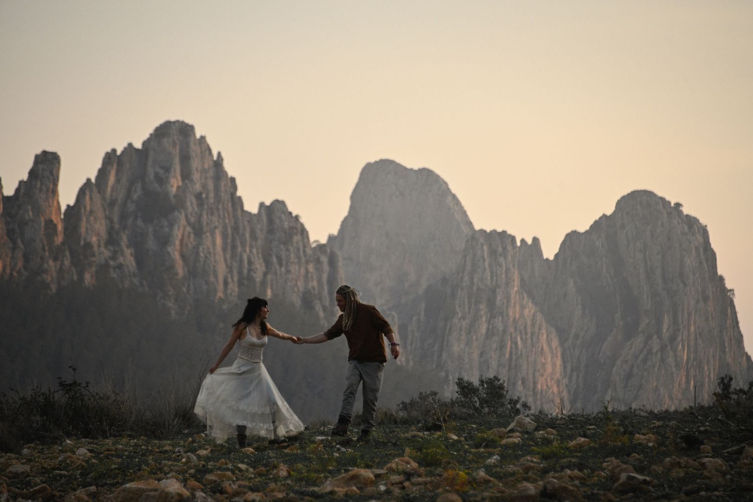 Silhouettes dancing on mountain summit with dramatic jagged peaks of Dolomites rising against misty sunset sky.