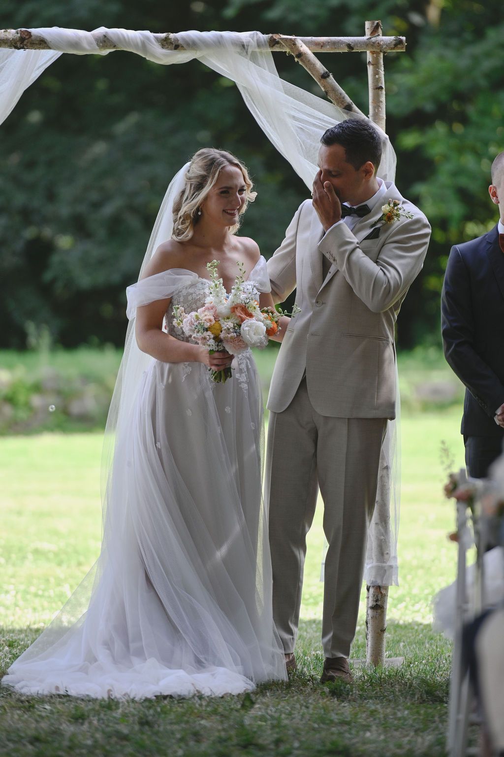 A couple shares a romantic moment during their outdoor wedding ceremony under a rustic wooden arch.