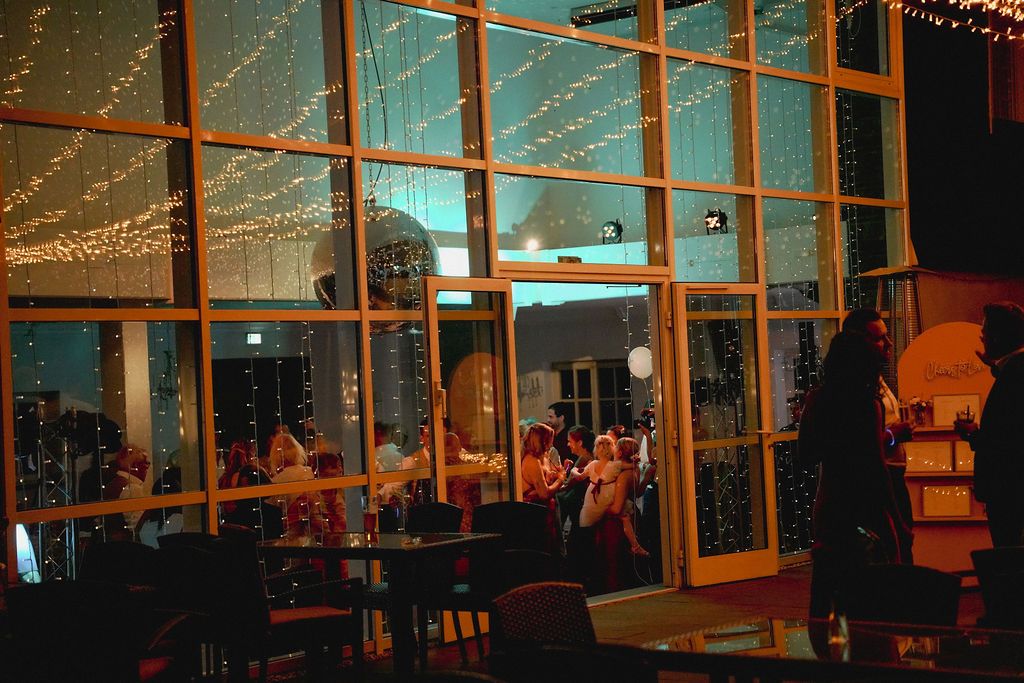A dimly lit restaurant interior with warm lighting and large windows overlooking a nighttime cityscape.