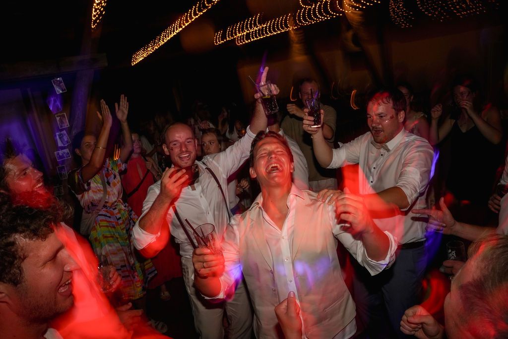 People dancing and celebrating at a dimly lit party with red and blue lighting effects.