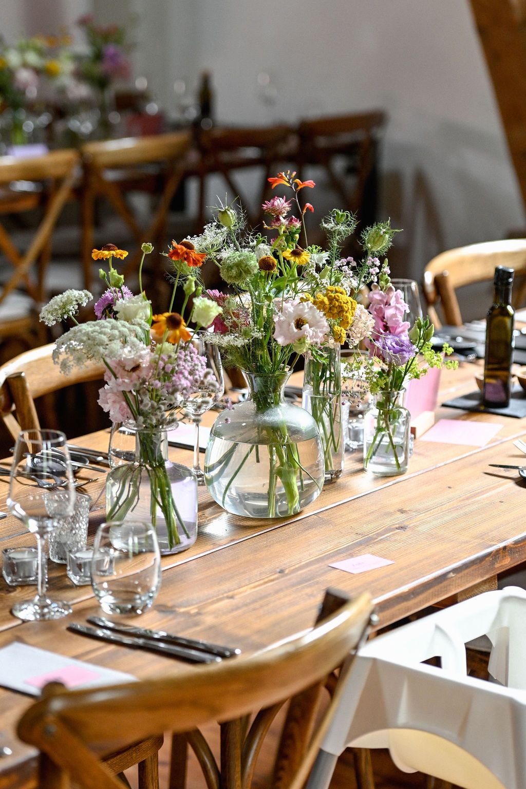 Rustic wooden dining table set for a casual gathering with small glass vases of colorful wildflowers and simple place settings.
