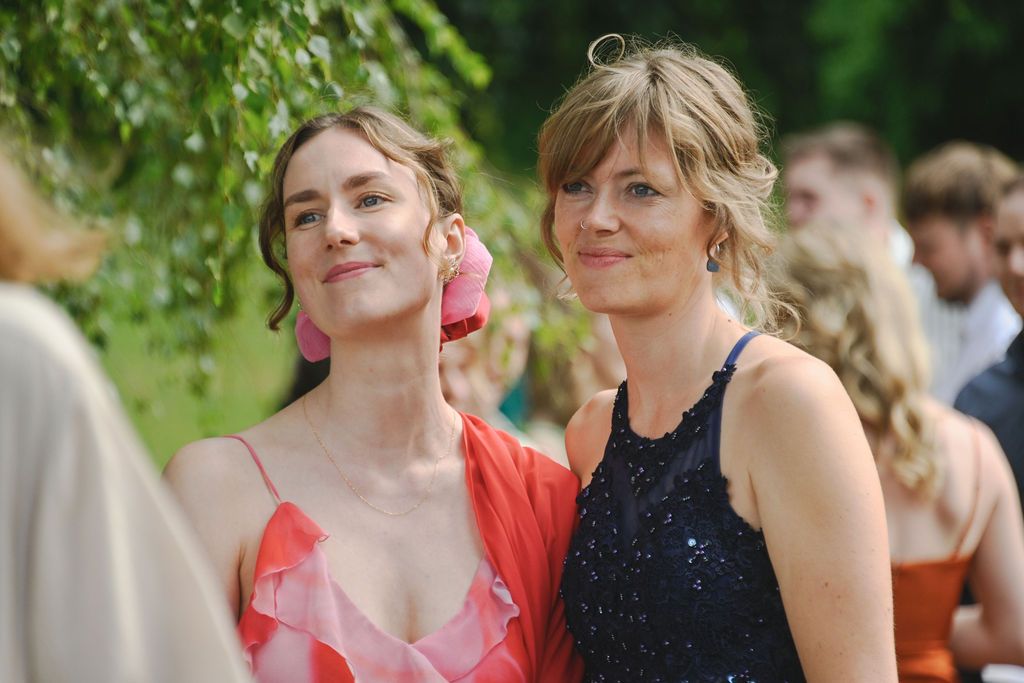 A group of people in formal attire gather outdoors for a celebration or event on a sunny day.