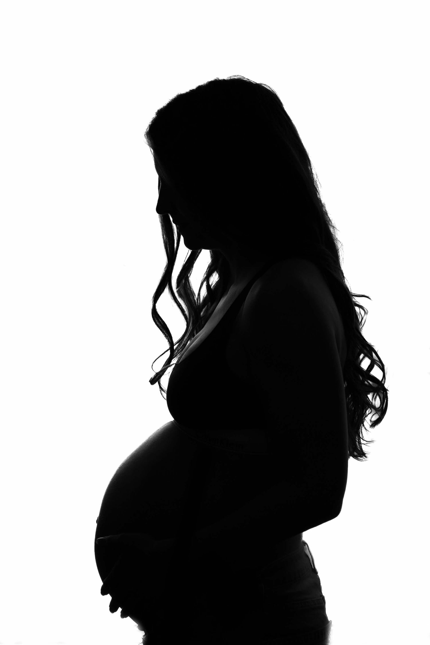 Elegant black and white silhouette of pregnant woman with long wavy hair cradling baby bump.