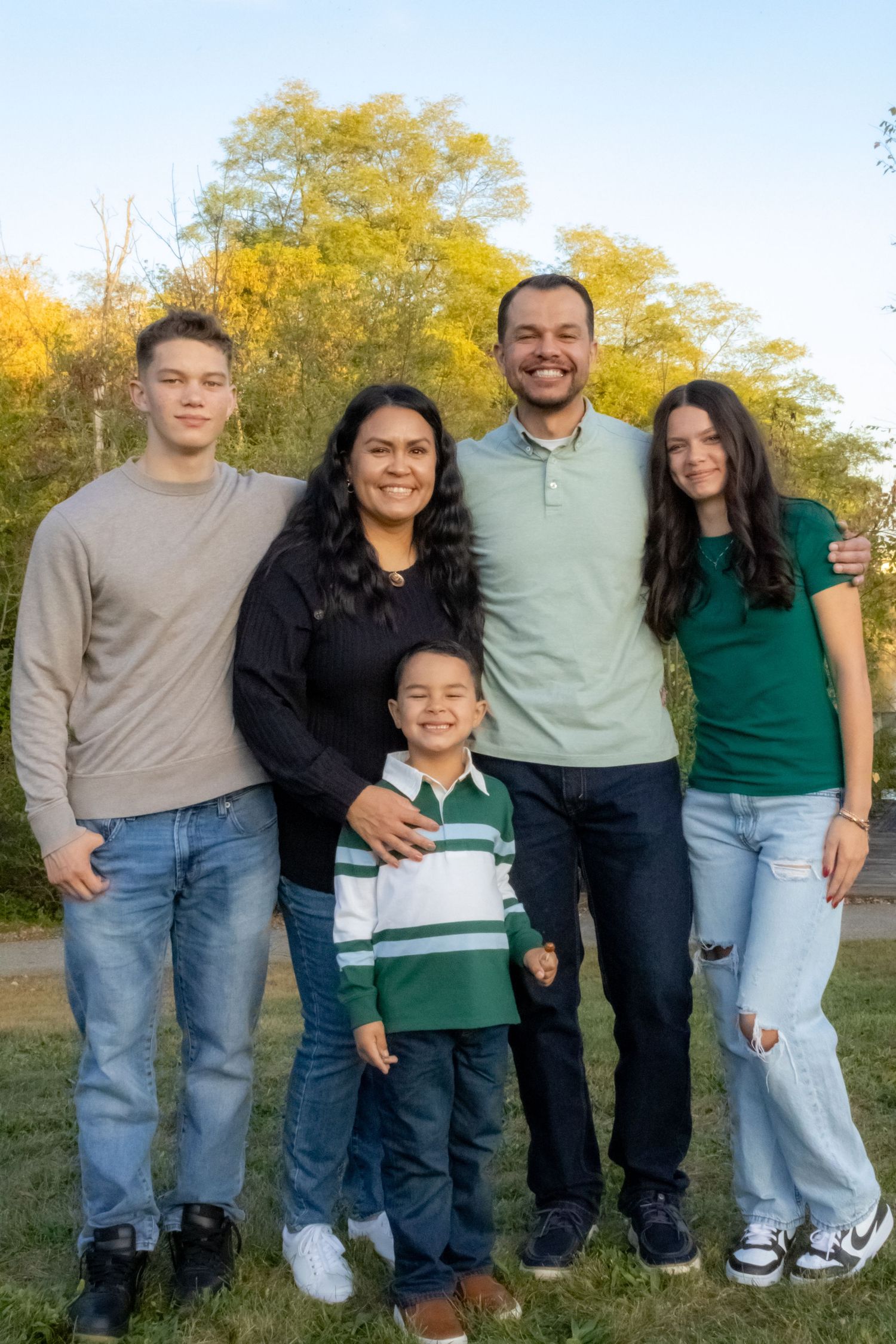Happy family of five smiling outdoors in autumn park with colorful foliage background.