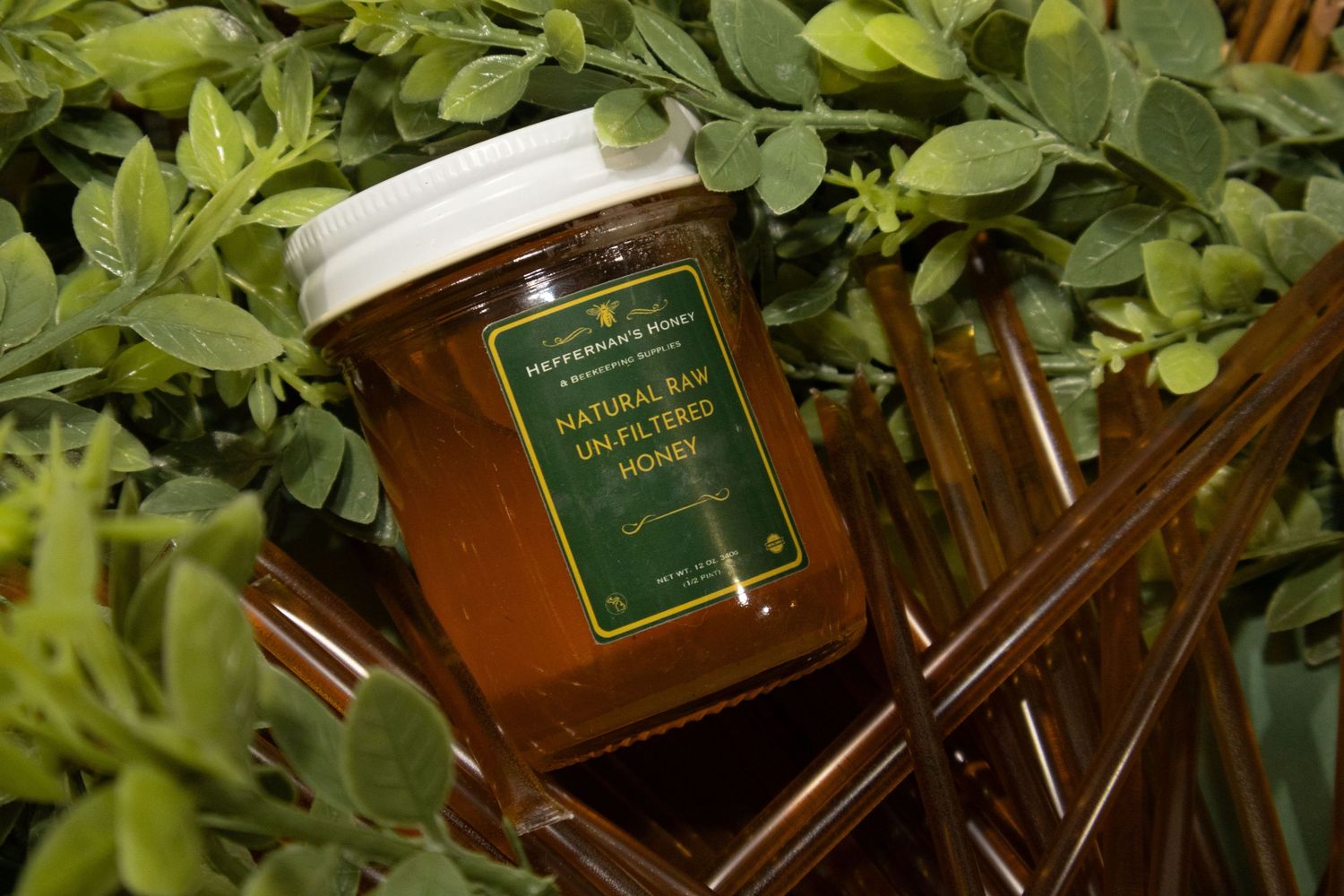 Jar of natural raw unfiltered honey surrounded by fresh green herbs and copper accents.