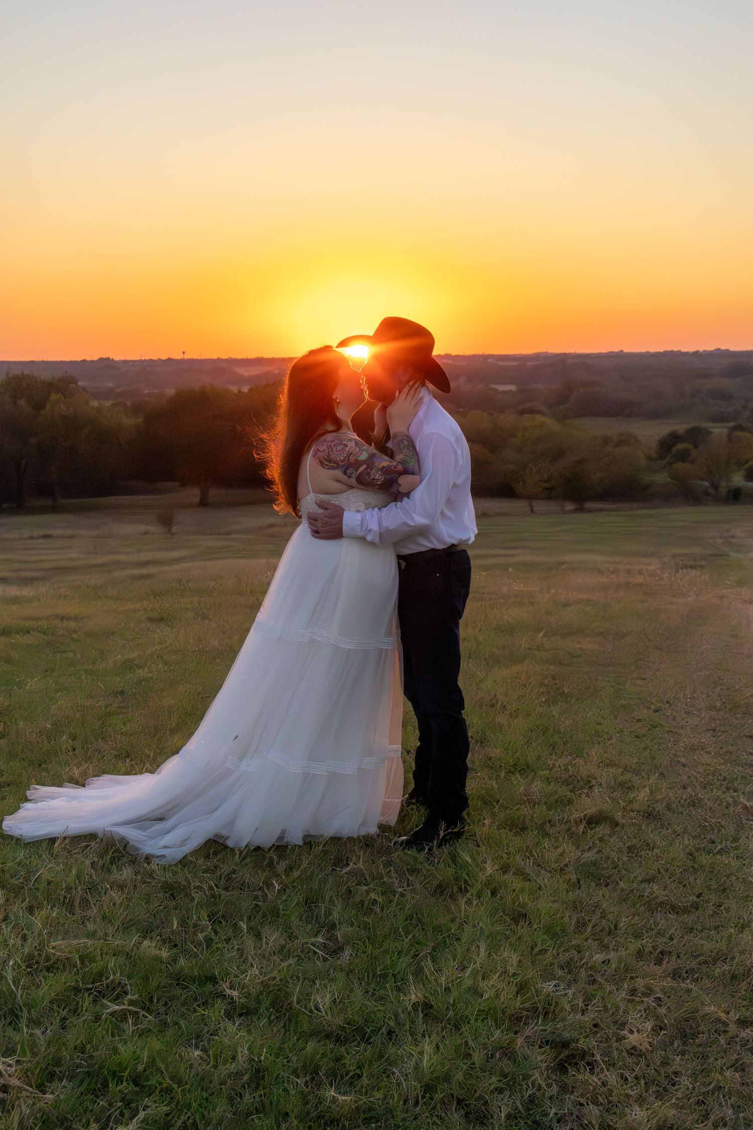 Bride and groom kissing at sunset in a green field during outdoor country wedding.