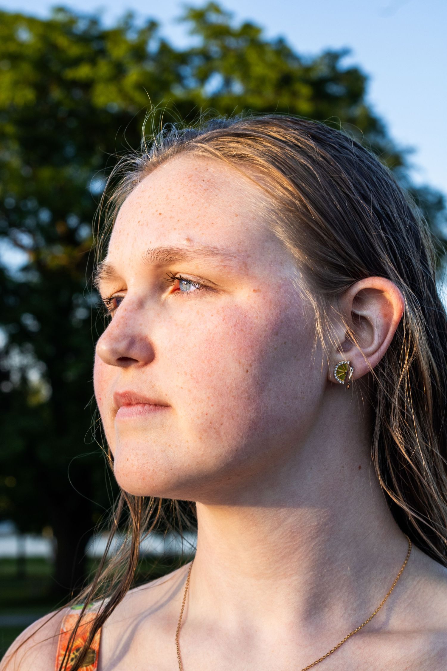Close-up portrait of young woman with freckles and wet hair in warm golden sunlight outdoors.