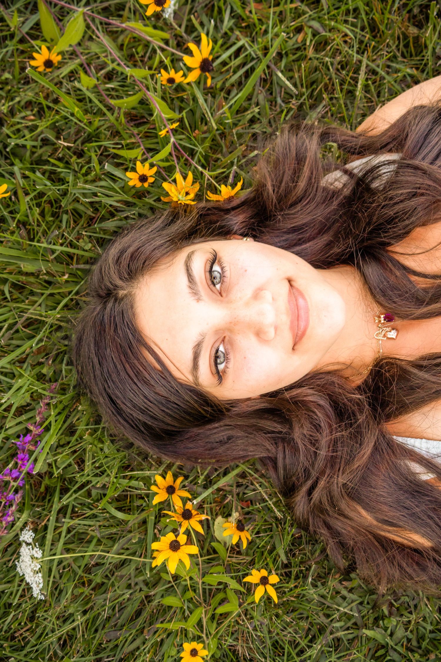 Young woman with long brown hair lying in green meadow surrounded by yellow wildflowers.