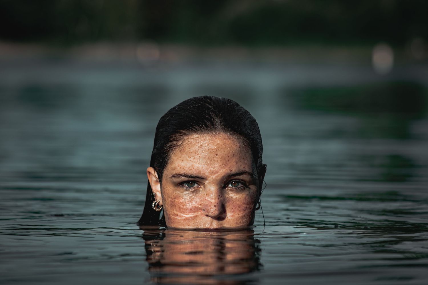 Dramatic portrait of a woman submerged in water with only her face visible above the calm lake surface.