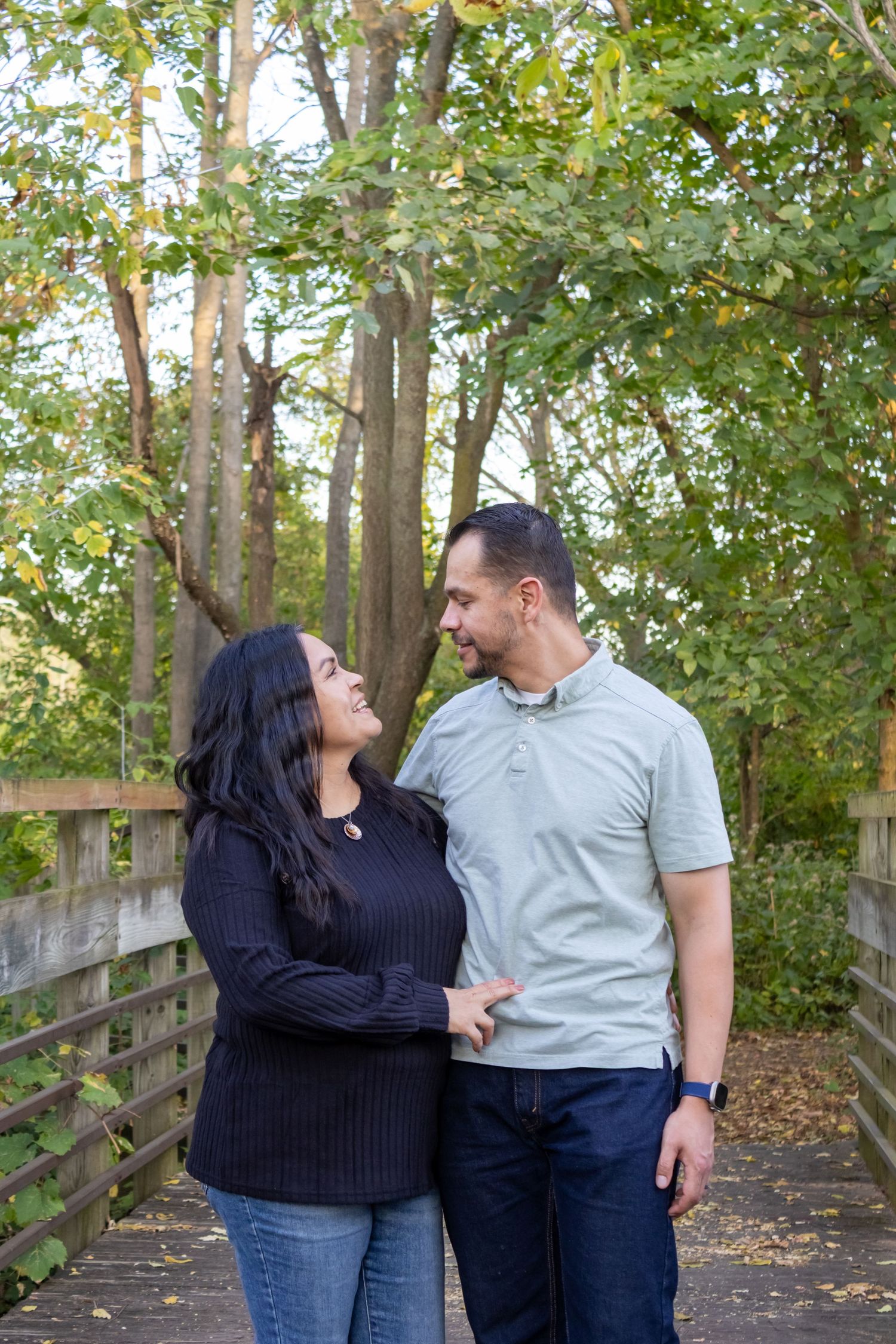Happy couple holding hands and smiling at each other on a wooden bridge in the park.