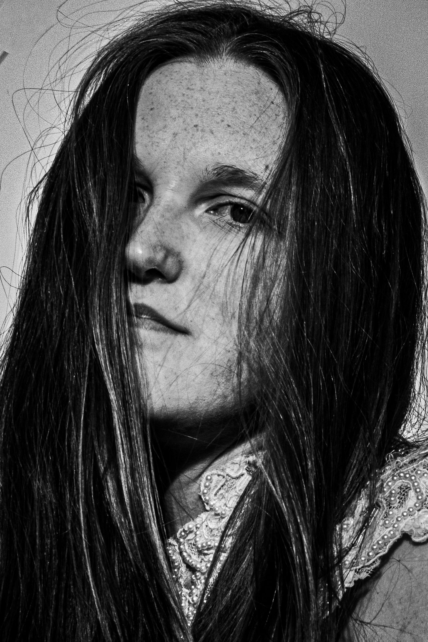 Black and white portrait of a young woman with long dark hair and freckles, gazing thoughtfully to the side.