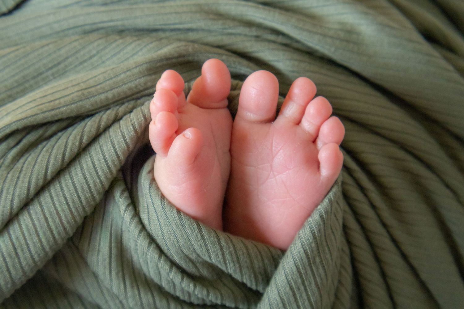Closeup of newborn baby feet wrapped in a soft green knit blanket.