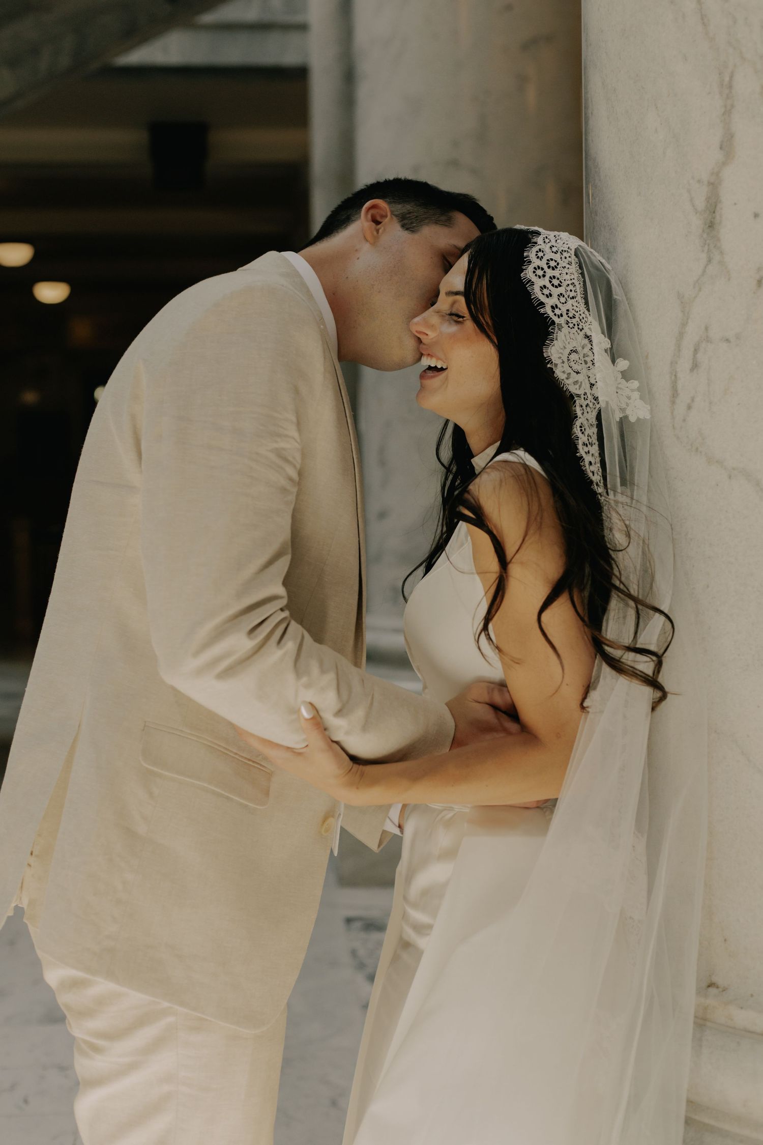 Wedding couple shares intimate moments against white pillars in natural lighting.