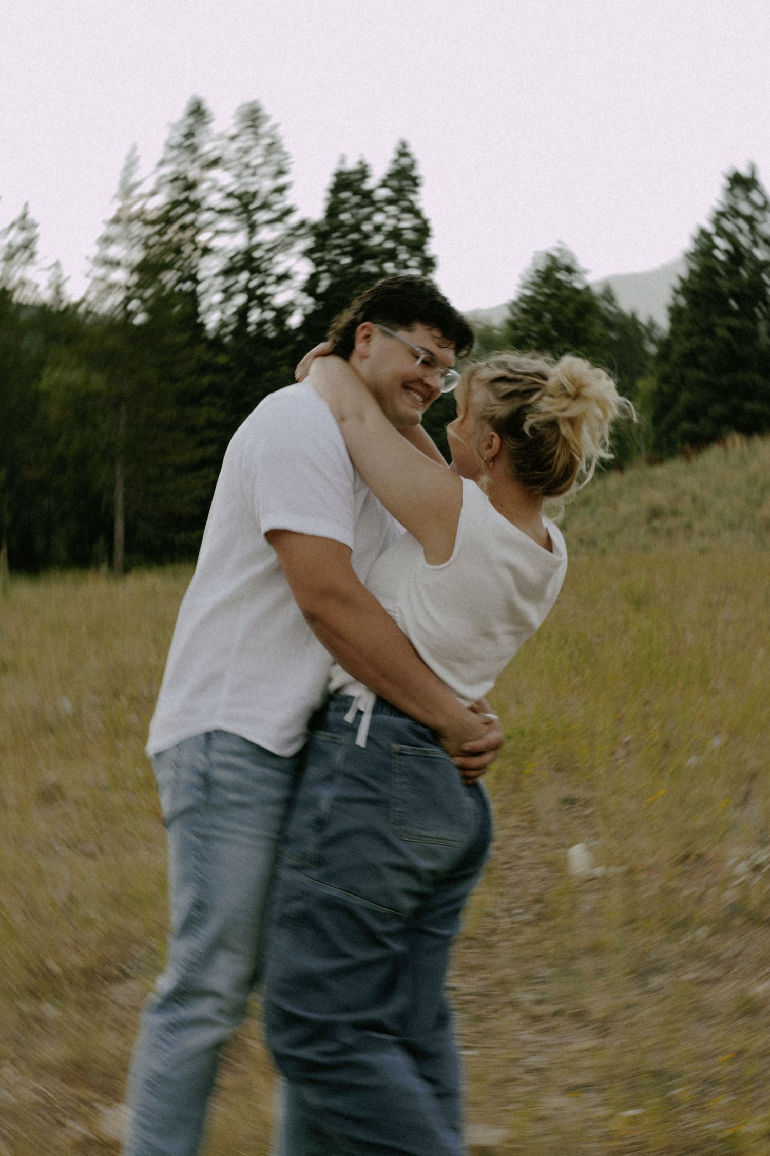A couple shares a tender embrace in a golden field with trees in the background.