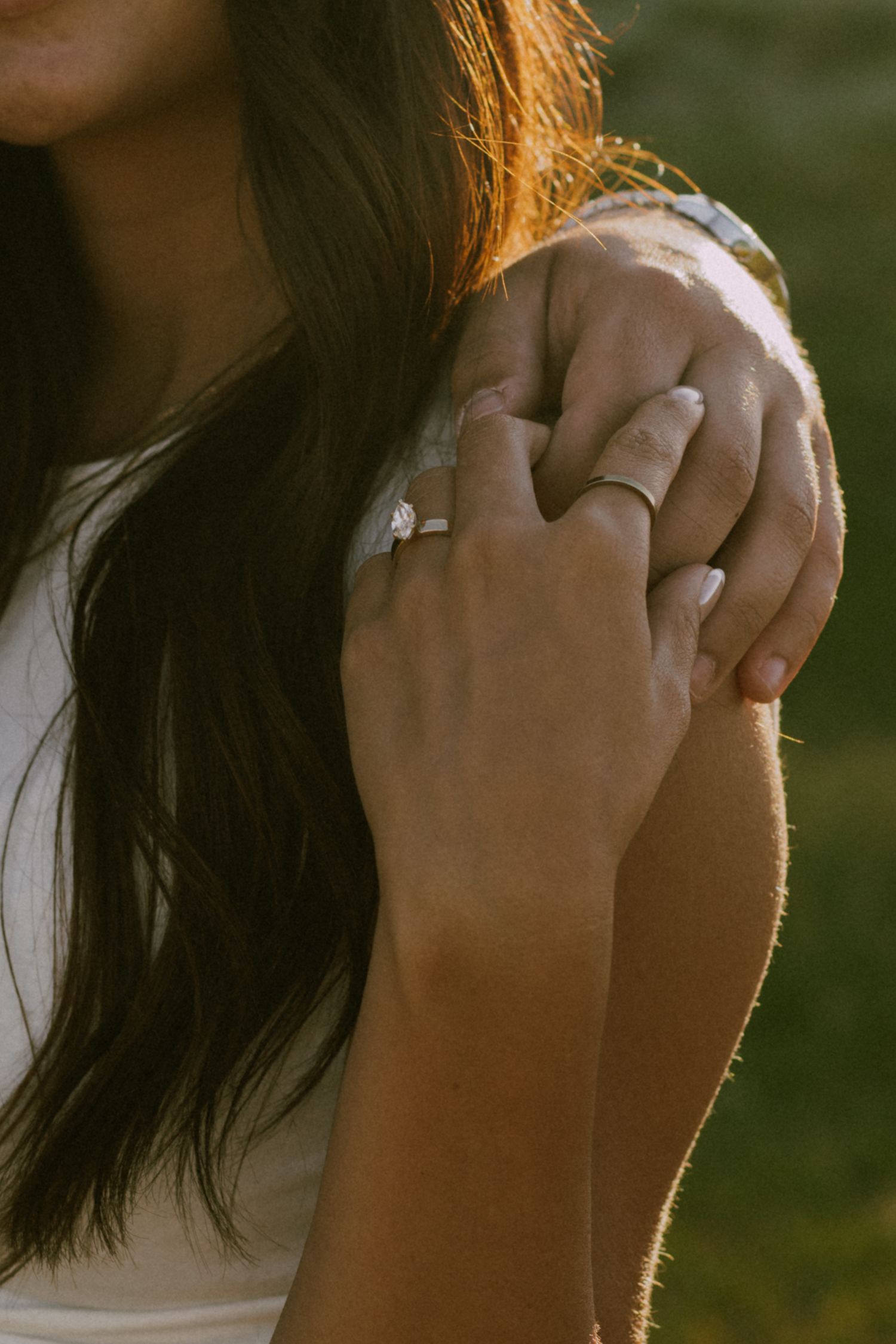 Close-up of hands showing engagement ring in warm sunlight.